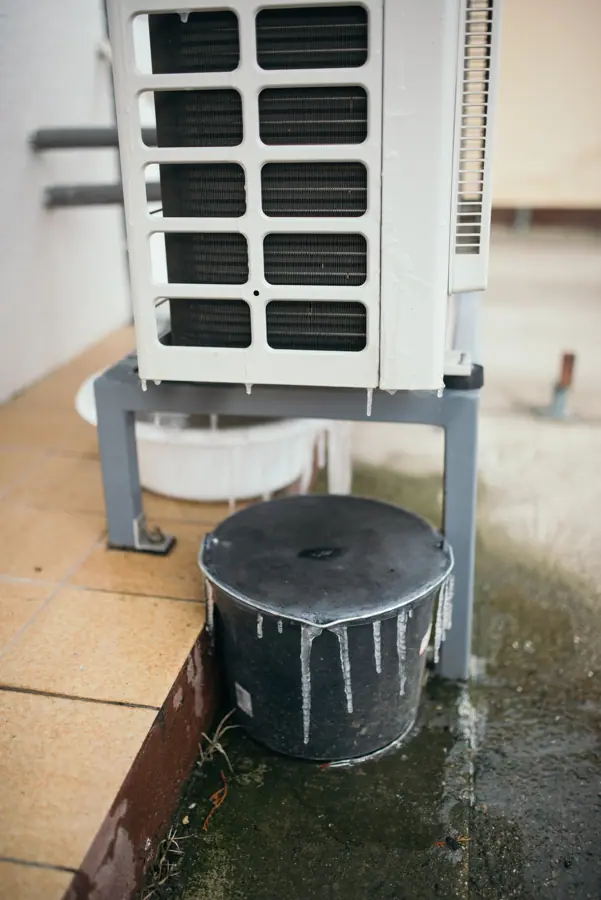 Water dripping from an air conditioning unit onto a black container at a residential property during a hot summer day