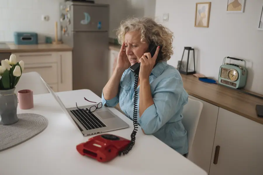 Elderly woman multitasking on the phone while managing tasks on her laptop