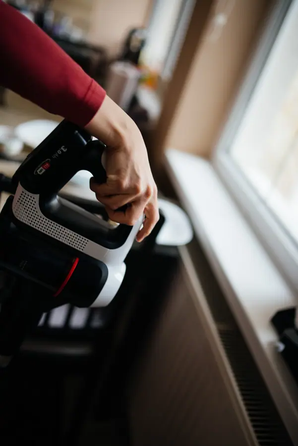 Cleaning a cozy indoor space with a handheld vacuum near a sunny window in a modern kitchen setting