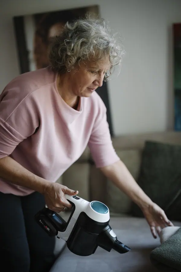 Middle-aged woman cleaning a couch with a handheld vacuum in a living room during the day