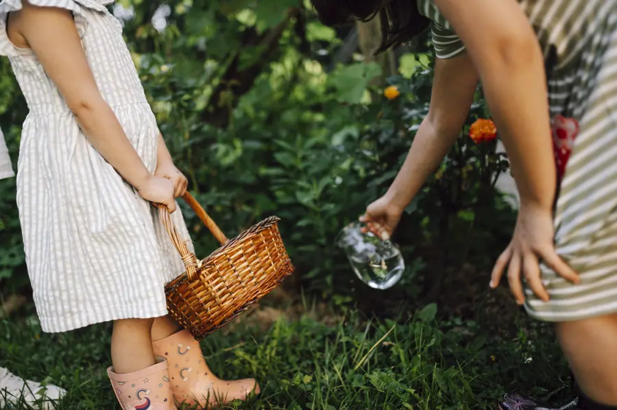 Children engage in gardening activities with a basket and watering can in a lush green backyard