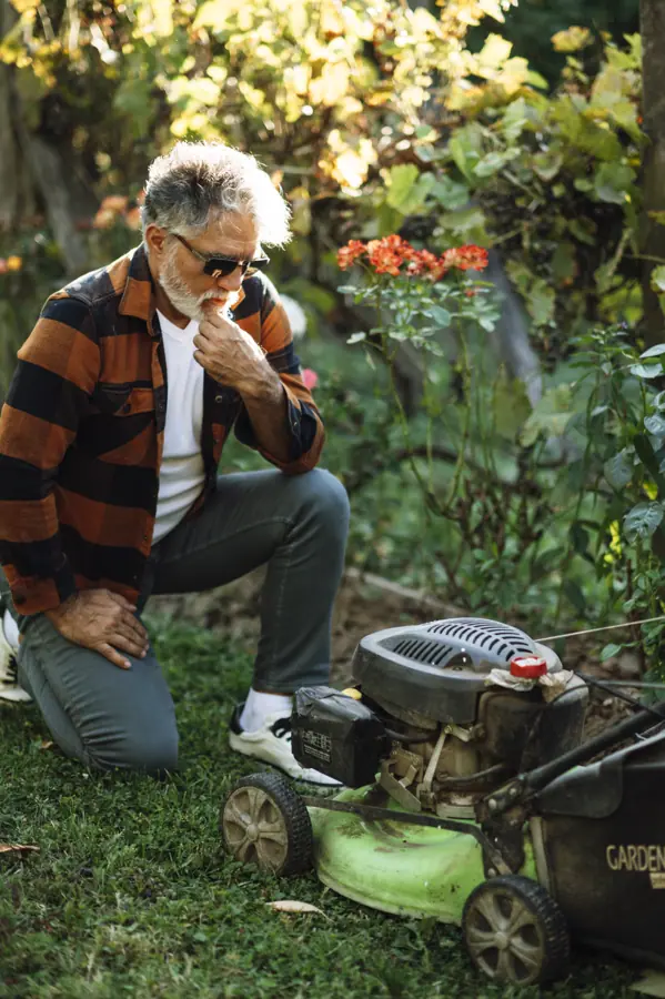 Man inspecting a lawnmower while kneeling in a vibrant garden