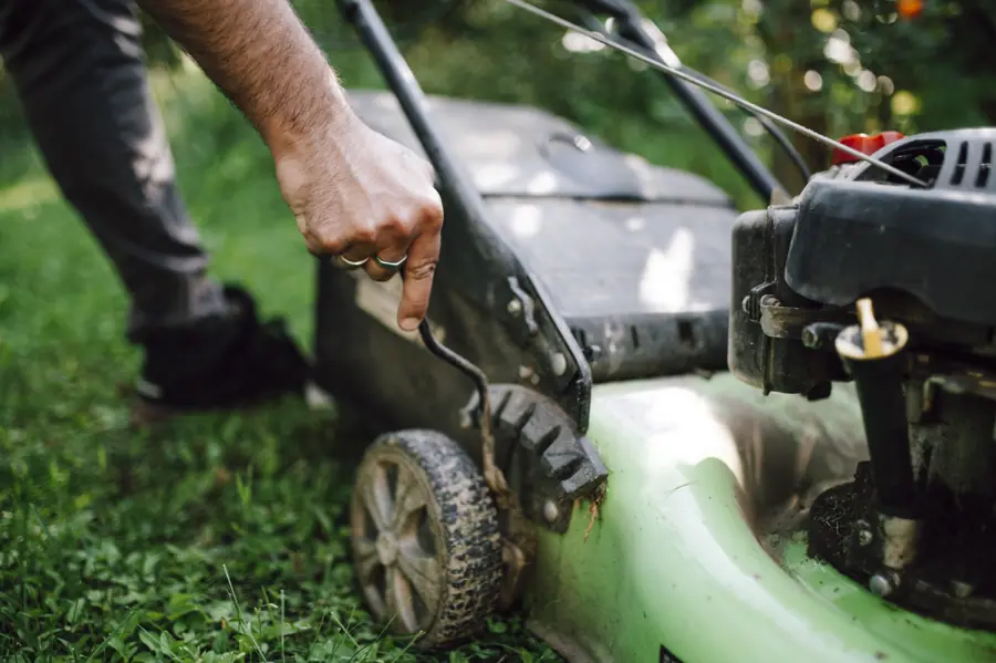 Man starting a lawn mower in a green garden