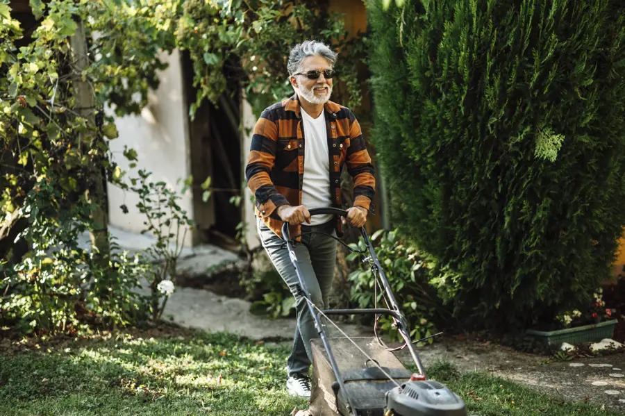 Senior man mowing the lawn in a backyard with greenery