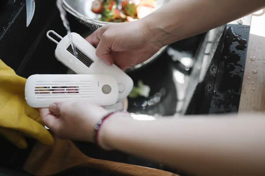 Hands hold kitchen cleaning tools while preparing food at a sink