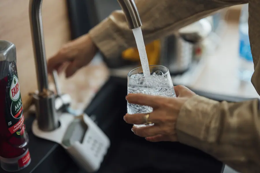 Person fills glass with water at kitchen sink