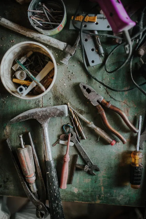 Various hand tools and hardware items scattered on an old green workbench in a workshop